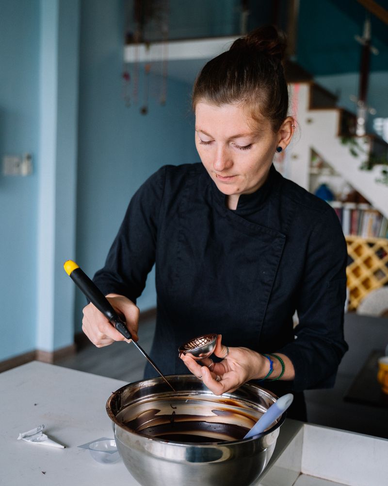Portrait de la Chef Élodie Martin en veste noire, concentrée sur le tempérage d'un chocolat.