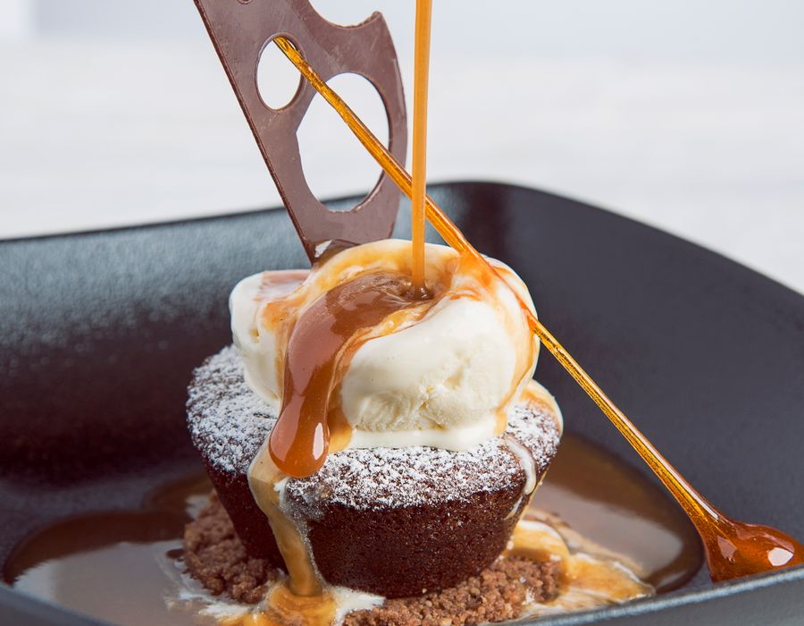 Soufflé au chocolat coulant, glace vanille et caramel beurre salé filant sur l'assiette noire.