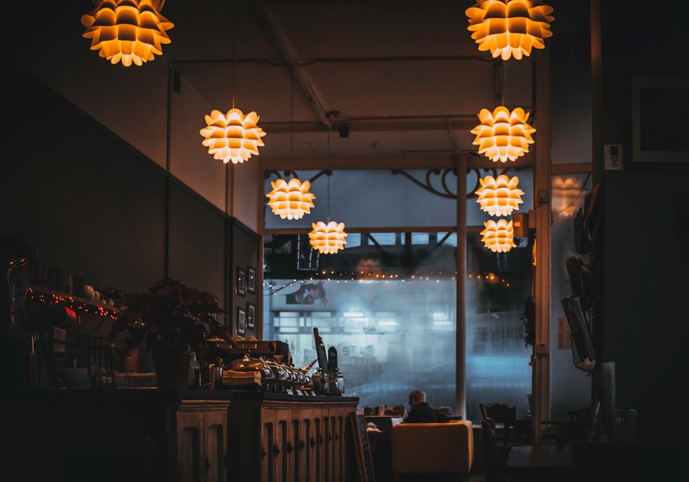 Salle du restaurant à la lumière tamisée, suspensions chaleureuses au-dessus des tables en bois.